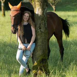 Reiterin neben ihrem Pferd an einem Baum stehend