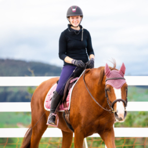 Reiterin lächelnd auf Pferd sitzend auf einem Reitplatz