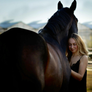 Reiterin lächelnd an ihr Pferd vertraut angelehnt