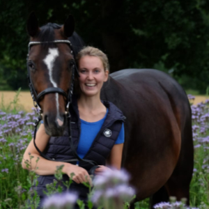 Reiterin lächelnd mit ihrem Pferd in einem Blumenfeld